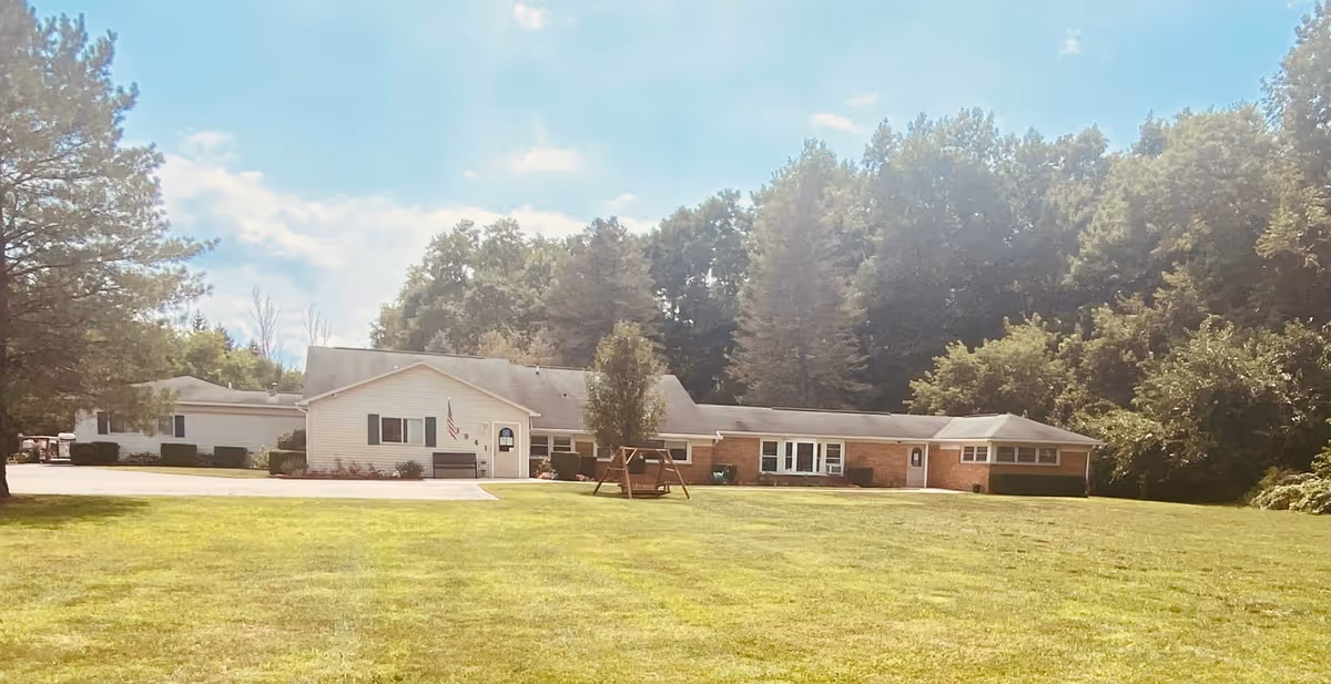Single-story light-colored building with a large front lawn, trees behind, and a wooden swing in front.