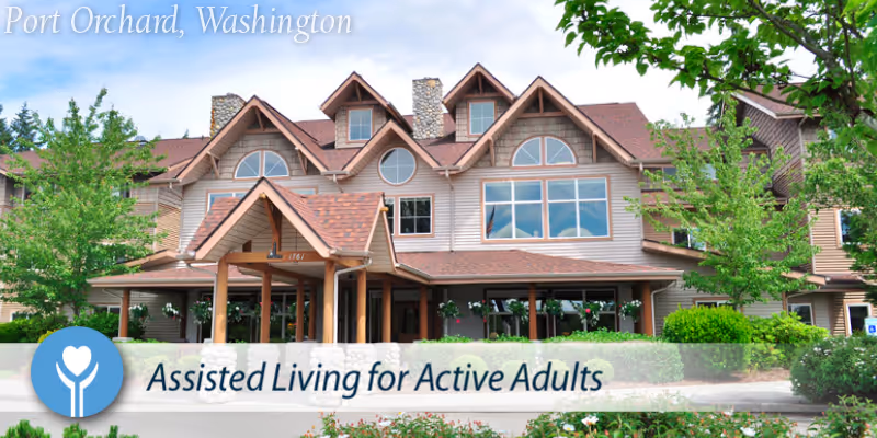 Exterior view of a large, multi-story assisted living facility building with a peaked roof and multiple windows, surrounded by greenery and trees under a blue sky with clouds. Text overlay reads 'Assisted Living for Active Adults' and 'Port Orchard, Washington'.