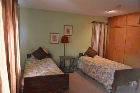 Two twin beds with floral quilts flank a central nightstand and lamp in a bedroom.