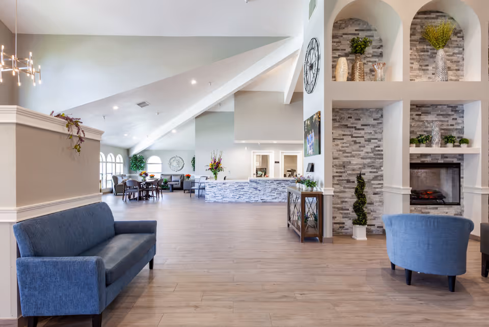 Spacious senior living facility lobby with blue seating, a stone fireplace, and modern decor.