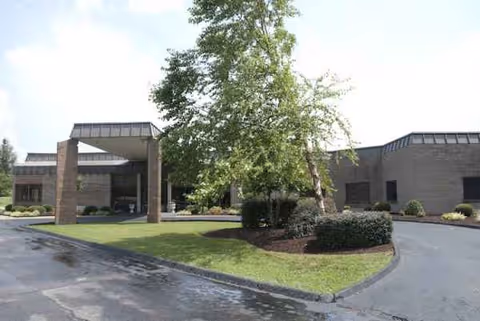 Exterior view of NHC Healthcare Scott entrance with driveway, trees, and landscaped island.