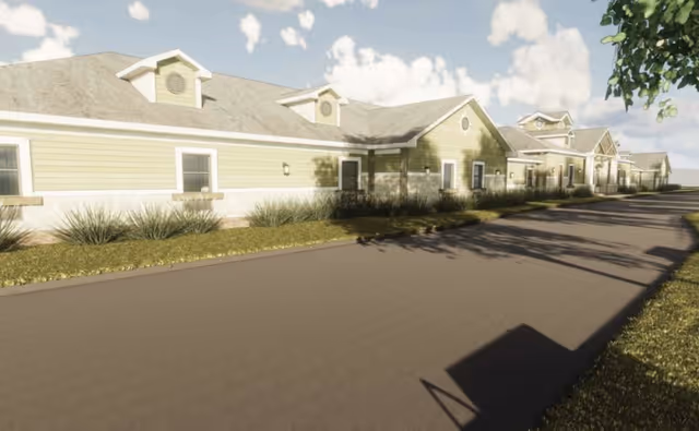 Long single-story assisted living building with dormer windows, landscaped beds, and a driveway under a partly cloudy sky.