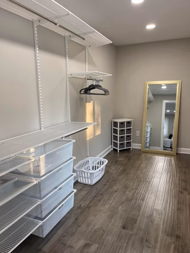 Empty walk-in closet/dressing room with shelving, hanging racks, mesh storage drawers, a laundry basket, and a full-length mirror.