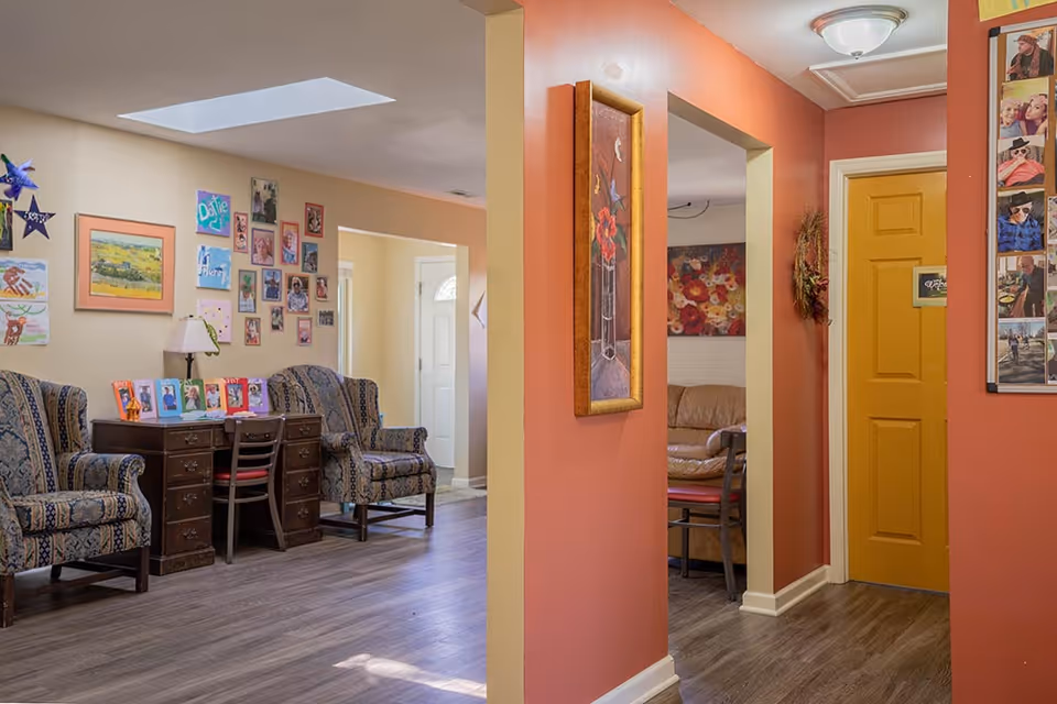Cozy senior living facility lounge with chairs, a desk, wall art, and a colorful hallway.