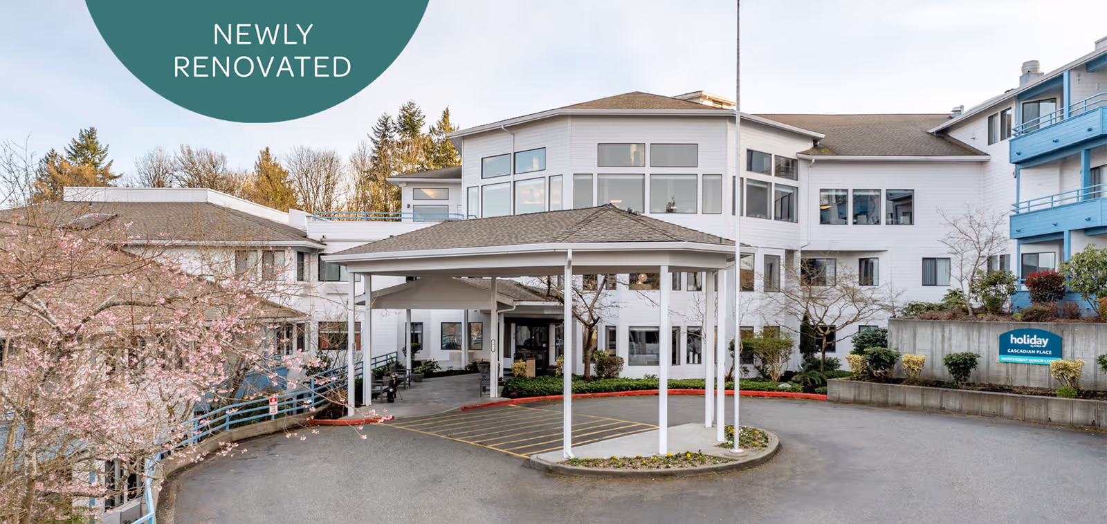 Front entrance of a multi-story senior living facility with a covered drop-off porte-cochère and landscaping.