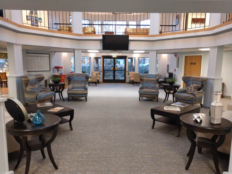 Spacious senior living facility common area with armchairs, side tables, and a television mounted above the main entrance.