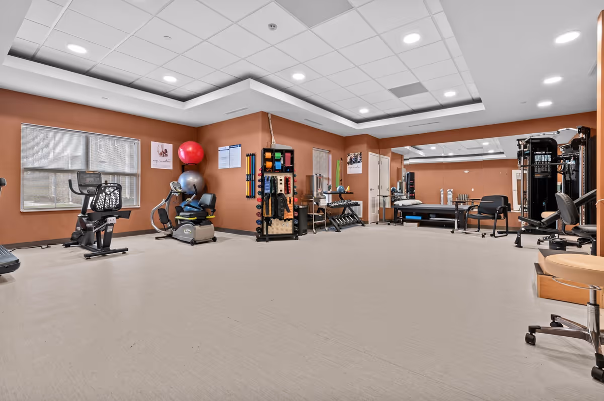 Spacious exercise and therapy room with cardio machines, weights, exercise balls, and a treatment table.