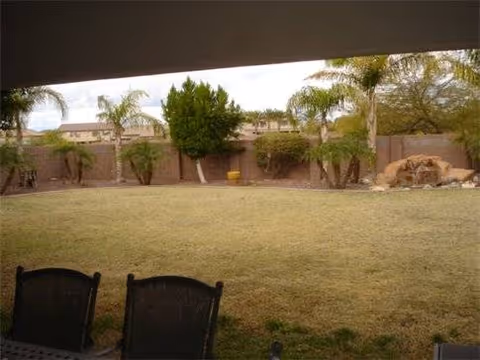 Shaded patio view of a grassy outdoor area with seating, trees, and a rock feature.