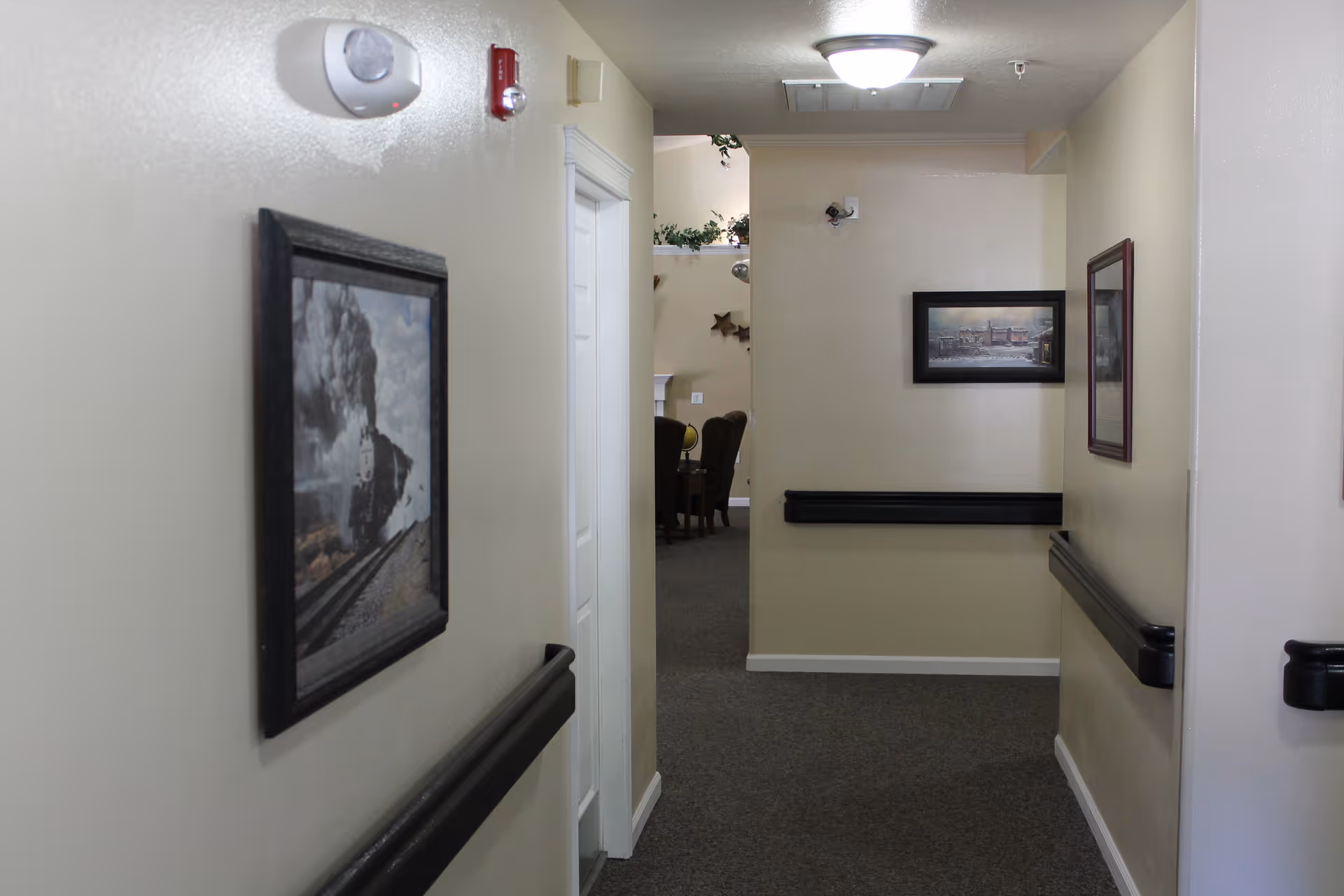 A carpeted interior hallway with framed pictures on the walls and black handrails leading to a seating area.