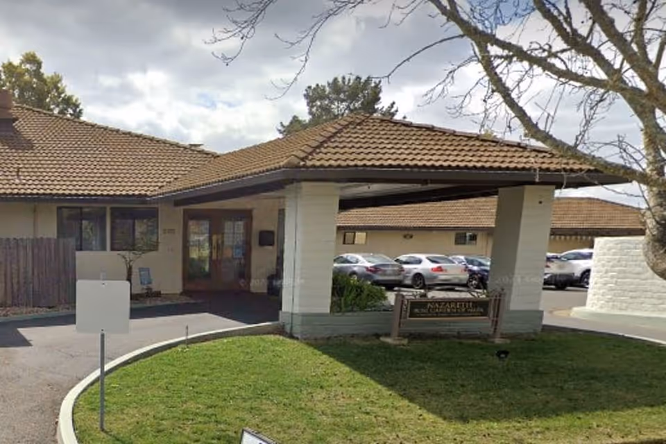 Exterior entrance of a single-story senior living facility with a covered drop-off, tiled roof, and a parking lot.