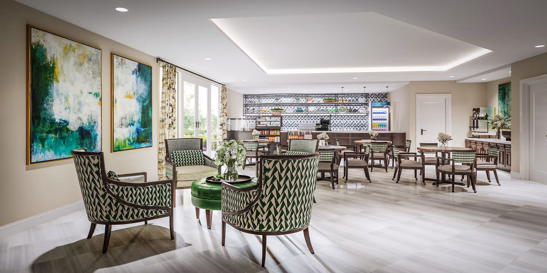 A bright and spacious dining and lounge area with multiple tables and chairs arranged neatly. The room features large windows with patterned curtains allowing natural light to fill the space. There are two large abstract paintings with green and blue tones on one wall. The back wall has a counter and shelves stocked with various items, including a coffee machine and a refrigerator. The floor is covered with light-colored tiles, and the ceiling has recessed lighting.