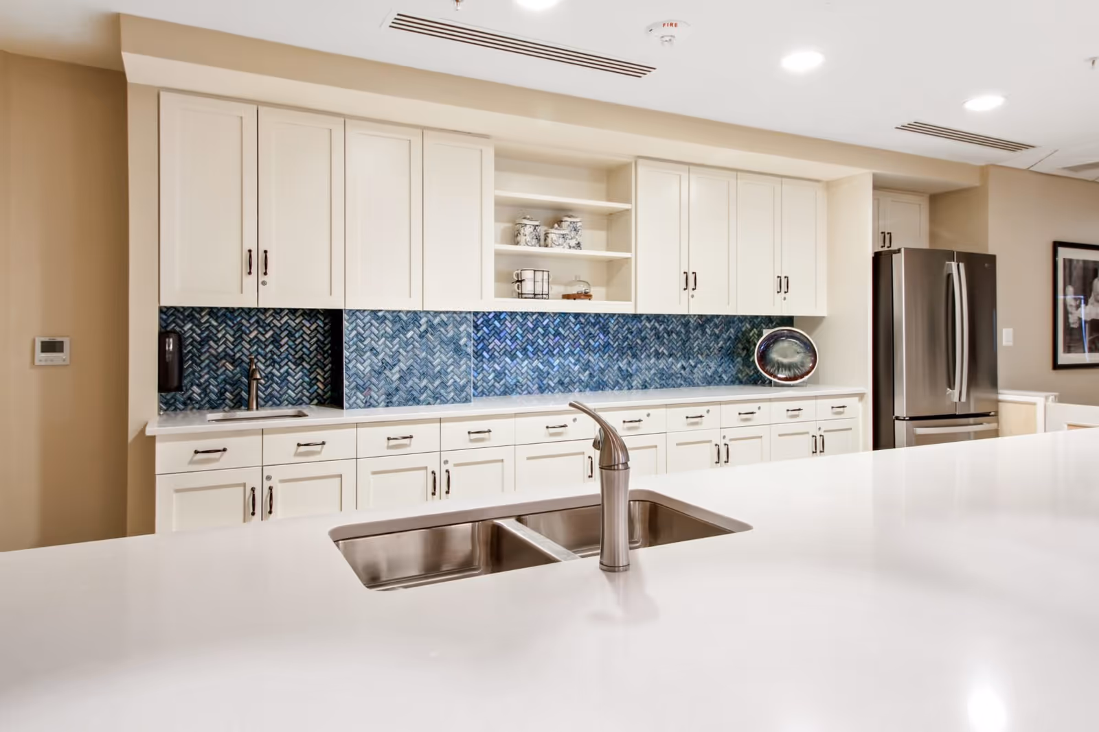 Bright modern kitchen with white cabinetry, blue herringbone tile backsplash, stainless steel fridge and a large island with a sink.