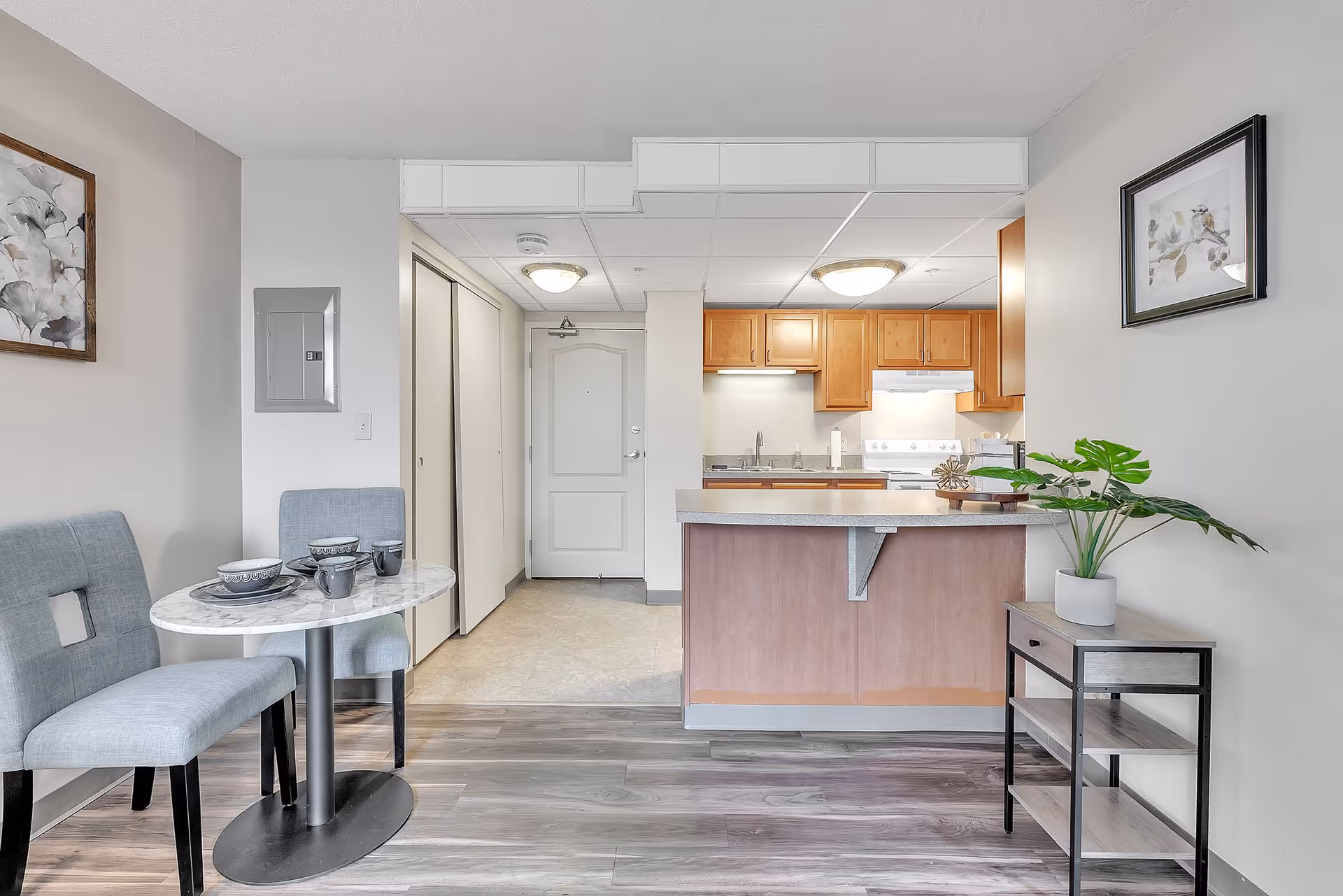 Open-plan studio interior showing a small kitchen with a breakfast bar, dining table, and entry door.