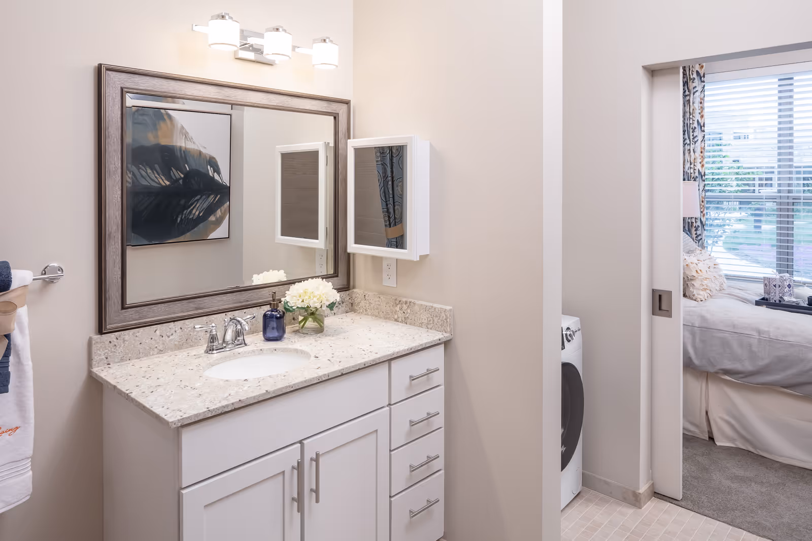 Bathroom vanity with a sink, mirror and countertop, opening into a bedroom where a washer is visible through a pocket door.