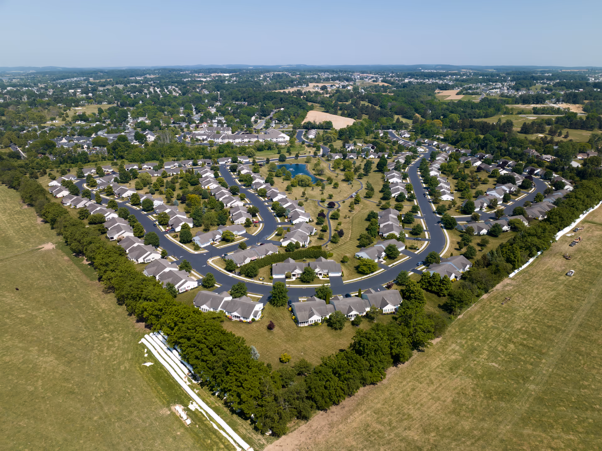 Aerial view of a residential community with single-story homes arranged along curving roads around landscaped green space and a central pond.