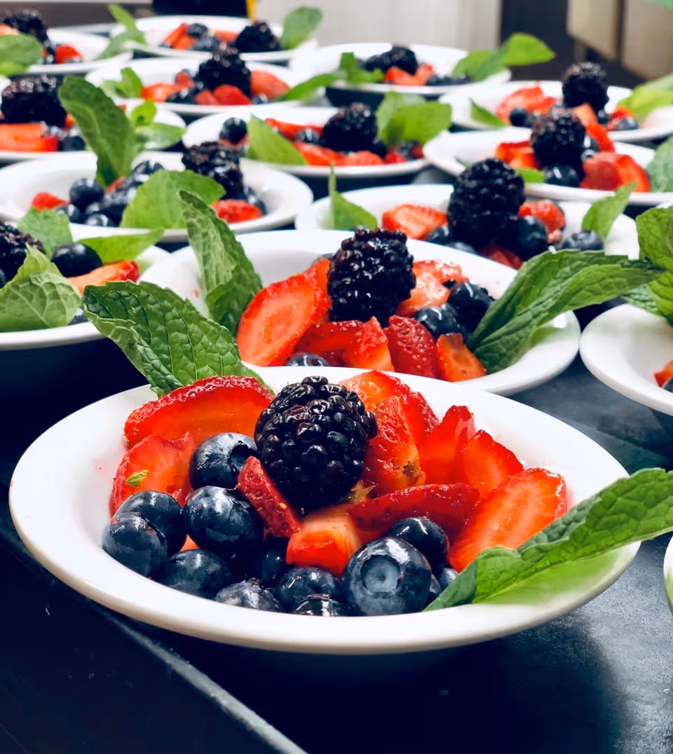 Bowls of fresh berries—strawberries, blueberries, and blackberries—garnished with mint leaves and arranged in rows.