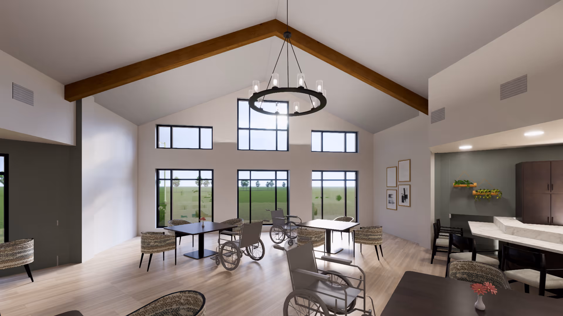A spacious, well-lit common area with high vaulted ceilings featuring wooden beams and large windows letting in natural light. The room contains several tables with chairs and wheelchairs around them, and a modern chandelier hanging from the ceiling. There is a counter area with bar stools and decorative plants on the wall.