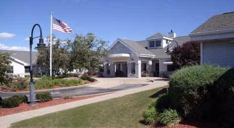 Exterior view of a senior living facility with a circular driveway and flagpole.
