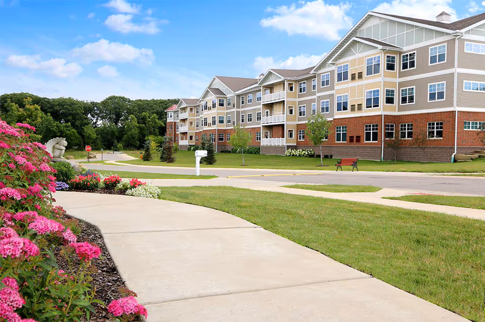 Front view of a multi-story senior living building with landscaped lawn, sidewalk, and flowerbeds.