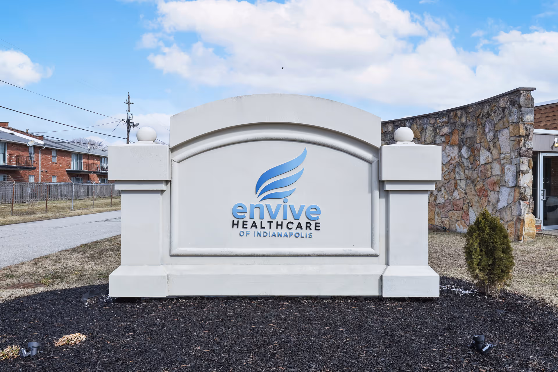 Monument sign reading "Envive Healthcare of Indianapolis" in front of a stone-faced facility under a blue sky.