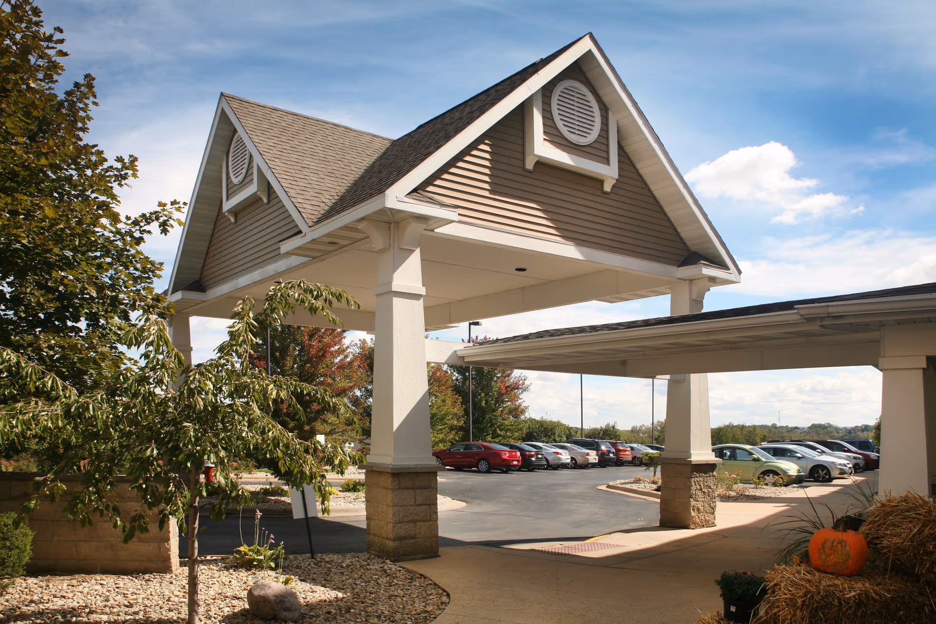 Covered entrance porte-cochere of a senior living facility with parked cars and landscaping.