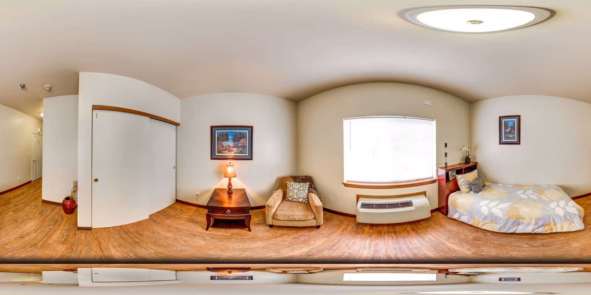 Bright studio bedroom with a bed, armchair, nightstand and lamp, window and closet.