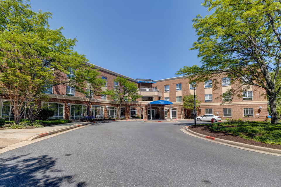 Front entrance of a three-story brick nursing and rehabilitation center with a circular driveway, canopy, and trees.