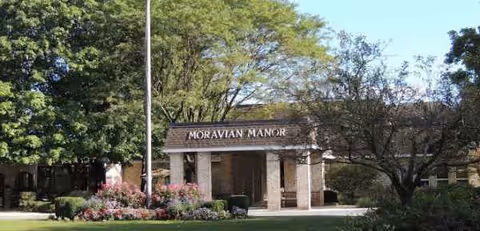 Front view of Moravian Manor entrance with landscaping and trees on a sunny day.