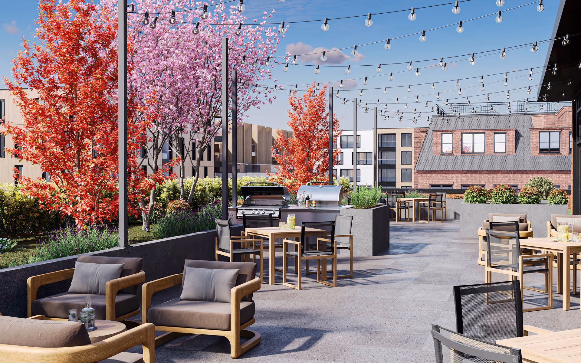 Outdoor patio area with modern wooden chairs and tables, string lights overhead, colorful trees with red and pink leaves, and two barbecue grills. The background shows a mix of modern and traditional buildings under a clear blue sky.