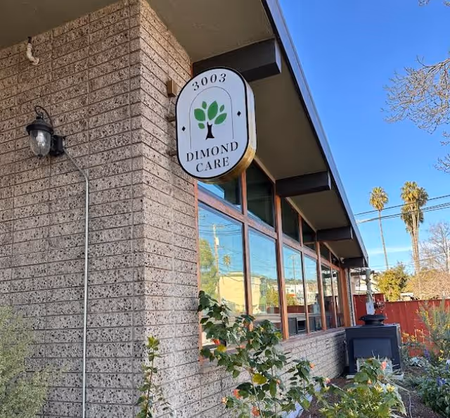 Front exterior of a single-story brick building with large windows and a hanging sign reading 'Dimond Care' featuring a tree logo.