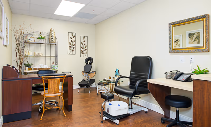 An interior treatment room with desks, wicker and leather chairs, decorative shelving, and a pedicure station.