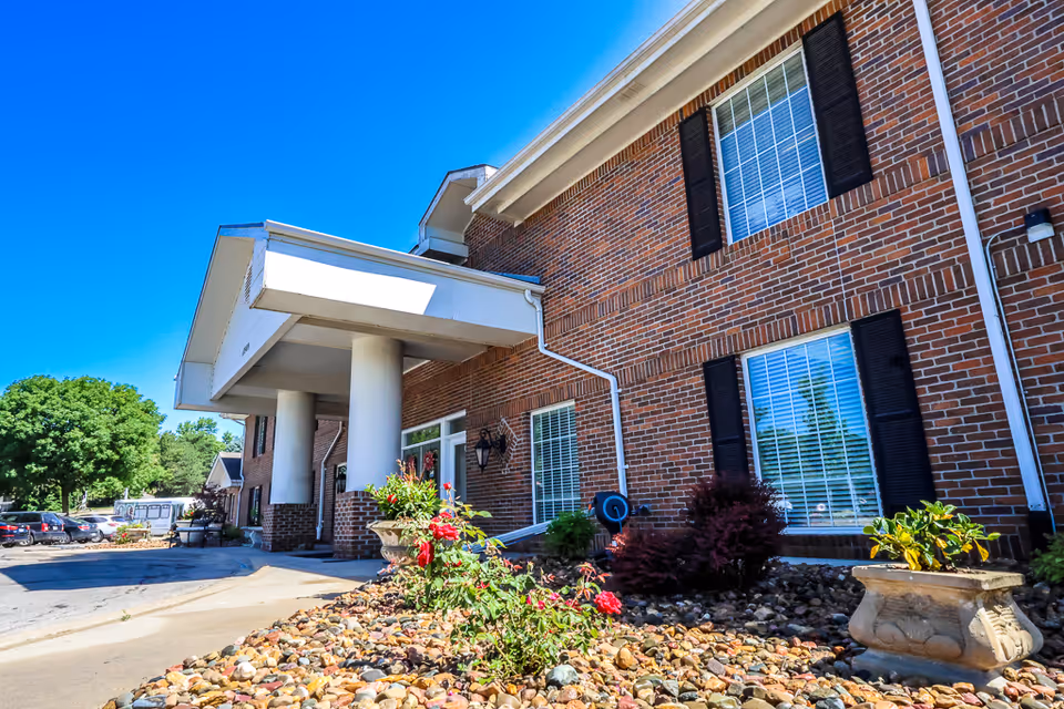 Brick senior living building exterior with entrance canopy, columns, windows, and landscaped rock garden.