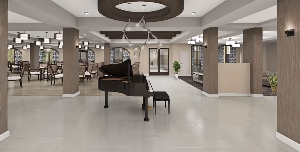 Spacious interior of a senior living facility featuring a black grand piano in the center of a tiled floor area. To the left, there is a dining area with multiple tables and chairs, illuminated by modern ceiling lights. The room has wooden columns and neutral-colored walls with large windows covered by patterned curtains. To the right, there is a seating area with sofas and plants, separated by more wooden columns.