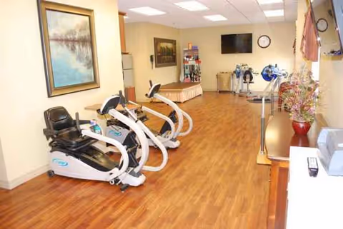 Interior fitness area in a senior living facility with exercise bikes and a wall TV.