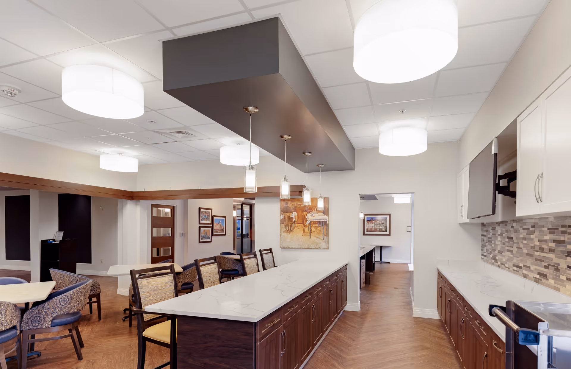 Communal kitchen and dining area with a long marble-topped island, pendant lights, seating, and cabinets.