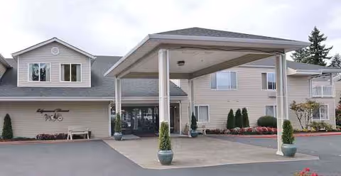 Exterior view of a senior living facility with a covered entrance and landscaping.