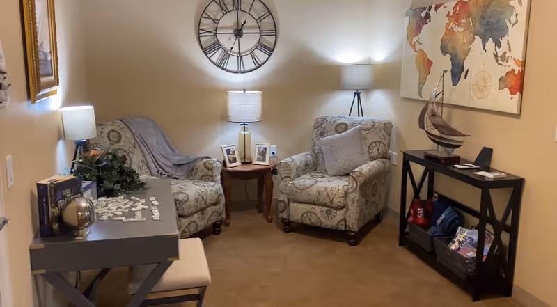 Cozy seating area with two patterned armchairs, side tables and lamps, a wall clock, console table and decorative accents.