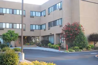 Exterior view of a beige brick senior living facility entrance with landscaped surroundings.