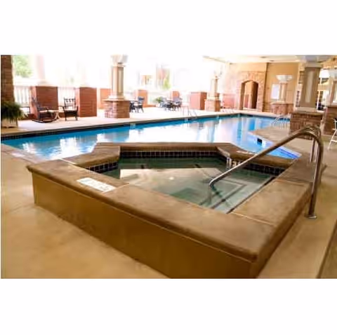 Indoor swimming pool area with a hot tub in the foreground, surrounded by brick columns and seating areas with chairs and tables in the background.