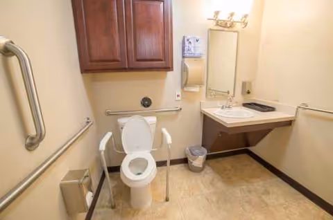 Accessible bathroom with toilet, grab bars, sink, mirror, and storage cabinets.