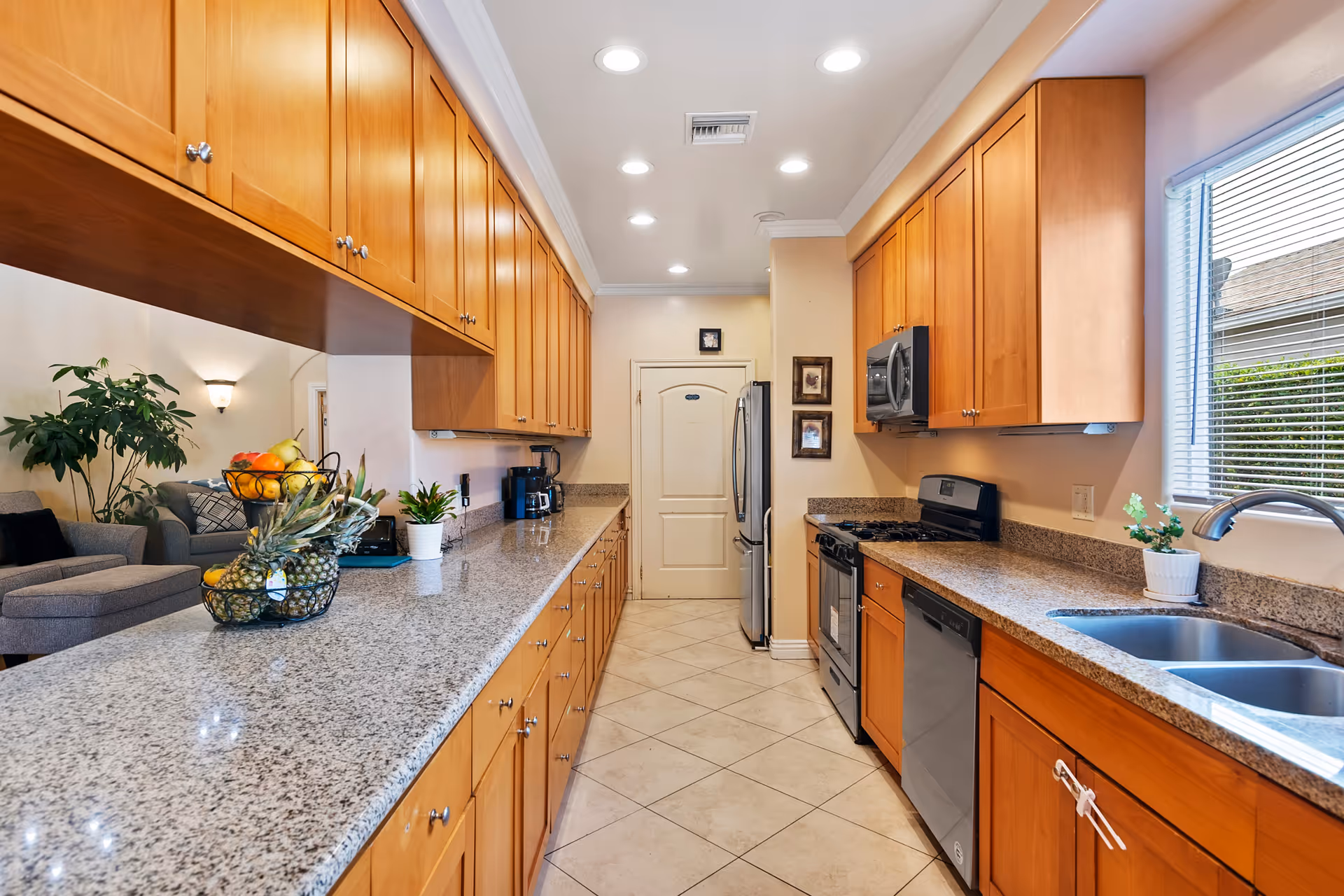 Long galley kitchen with granite countertops, wooden cabinets, stainless steel appliances and a sink by a window.