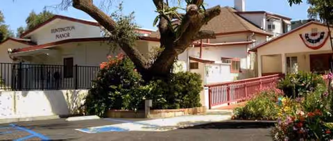 Exterior view of Huntington Manor facility with a large tree, ramp, and parking.