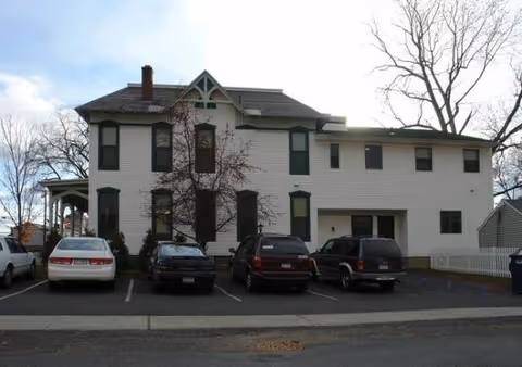 Two-story white building with a front parking lot and several parked cars.