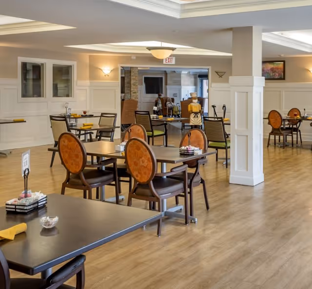Communal dining room with multiple set tables and upholstered chairs on a wood floor.