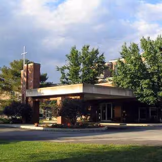 Front exterior view of a brick senior living facility with a flat canopy and surrounding trees.