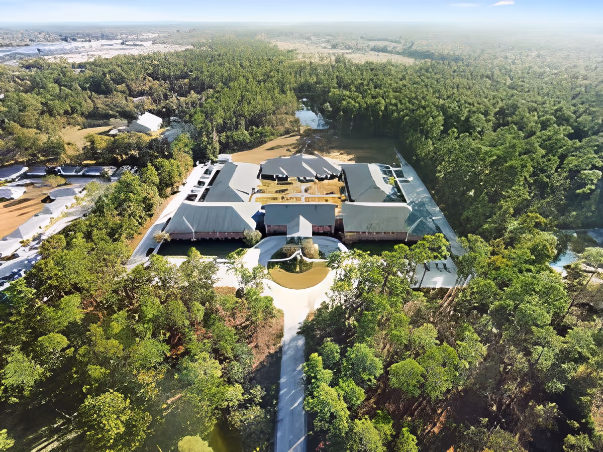 Aerial view of a single-story senior living complex surrounded by dense trees with a circular driveway leading to the central entrance.