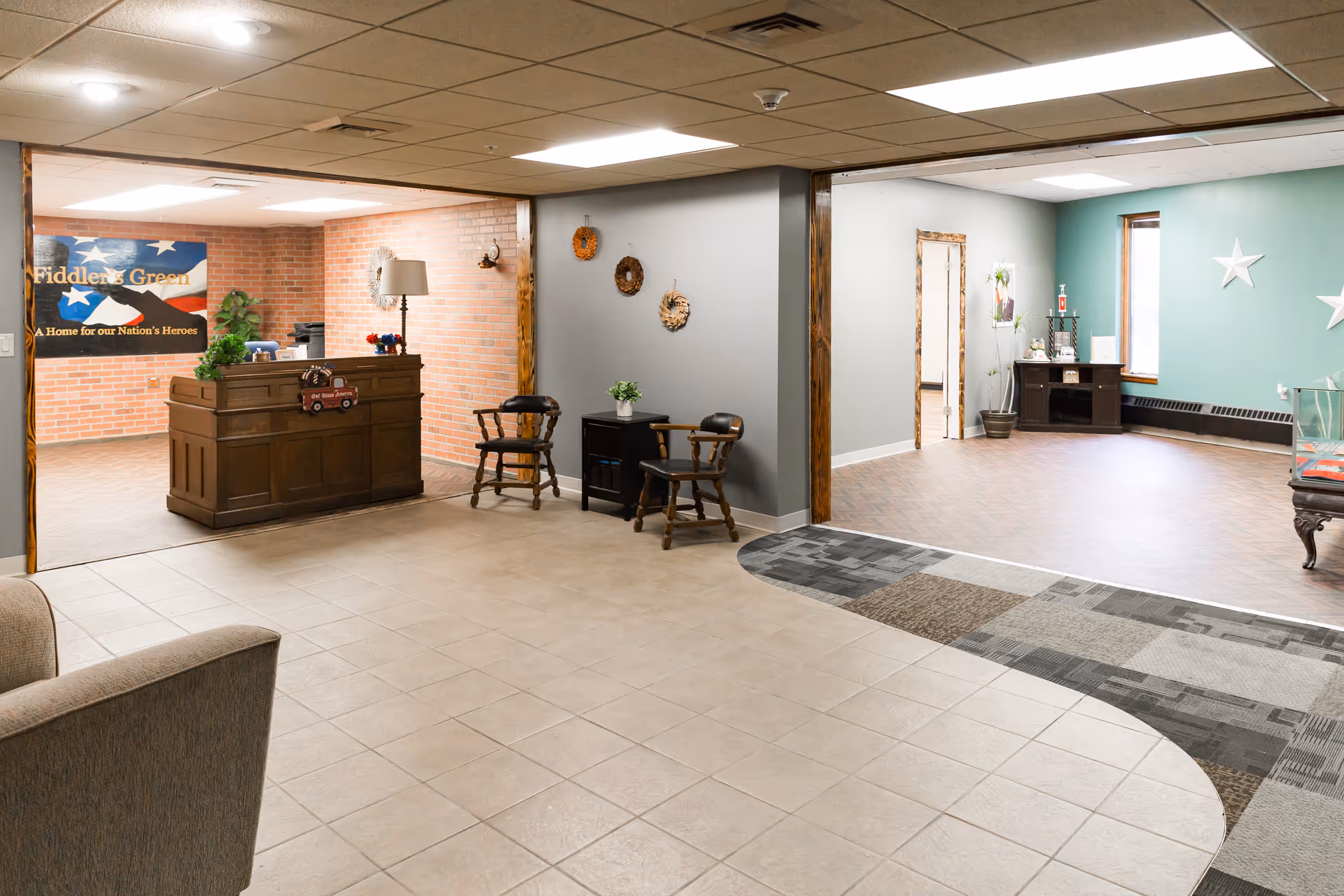 Lobby of a senior community showing a reception desk, seating areas, and adjoining rooms with tiled and wood floors.