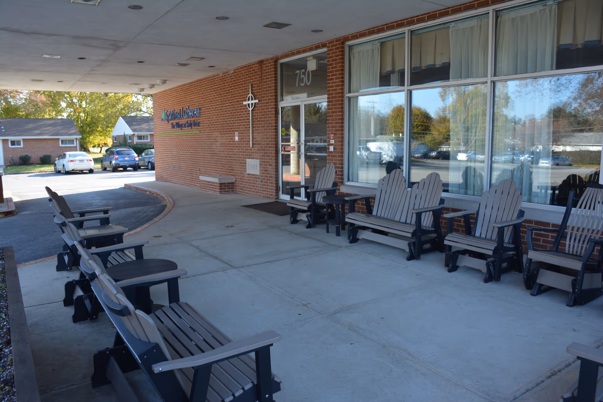 Covered brick entrance of Kelly Manor with rows of outdoor chairs and a glass entry door marked 750.