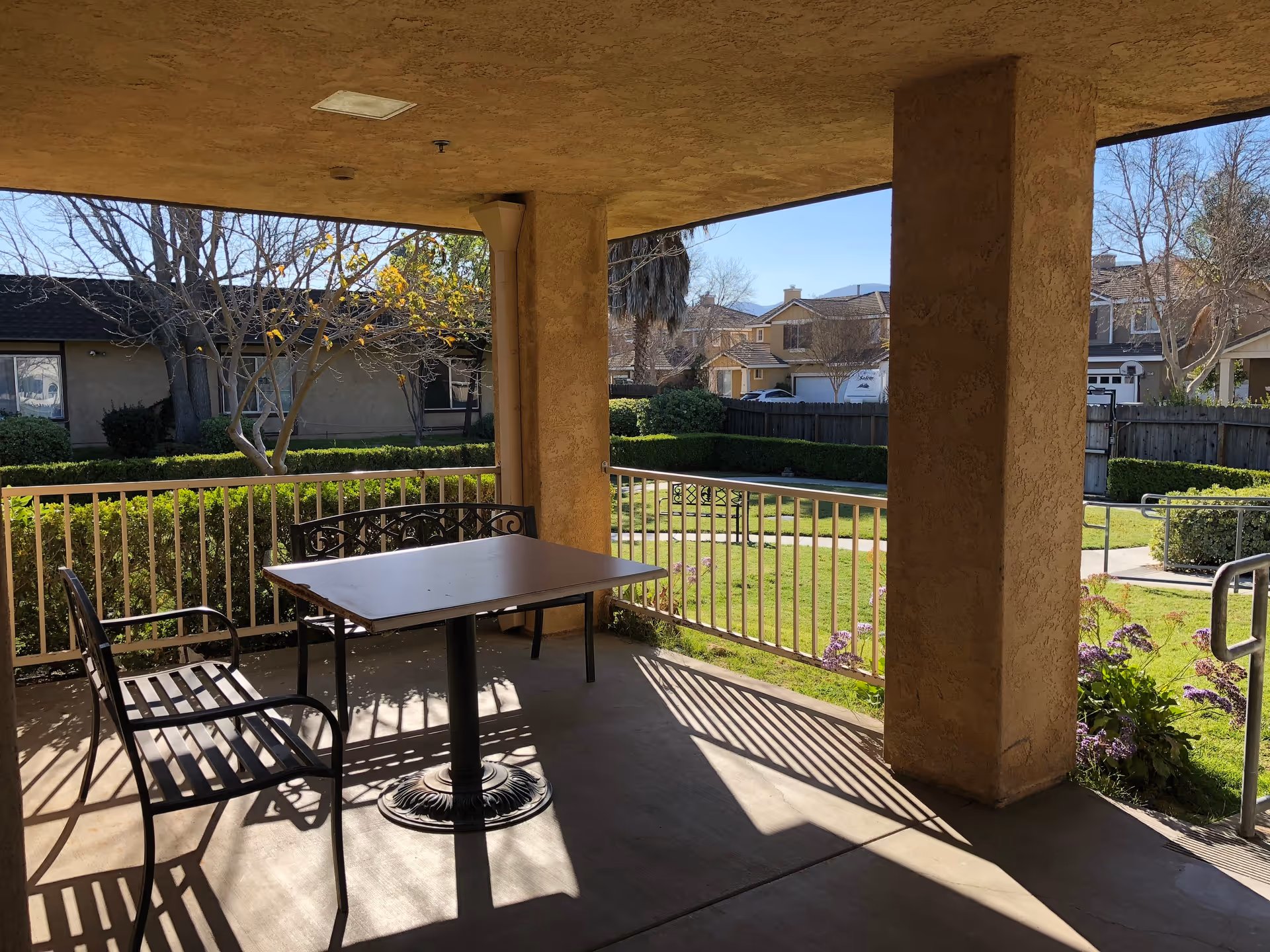 Covered patio with a table and metal chairs overlooking a grassy courtyard and nearby homes.