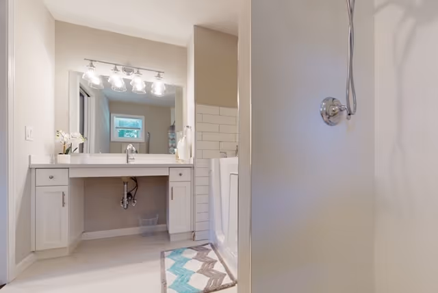 Bright bathroom with a single sink, large mirror, vanity lights, and a glass shower.
